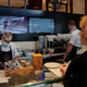 Masked chef prepares food for customer in fast-casual restaurant
